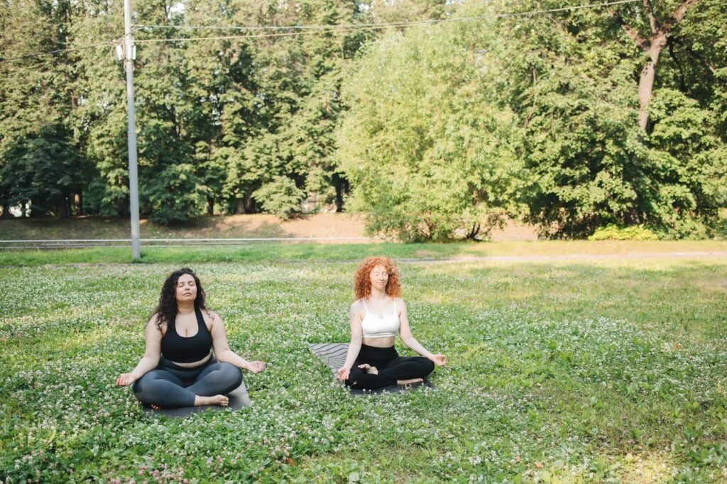 Two women meditating in a sunny park, practicing yoga for mental peace.